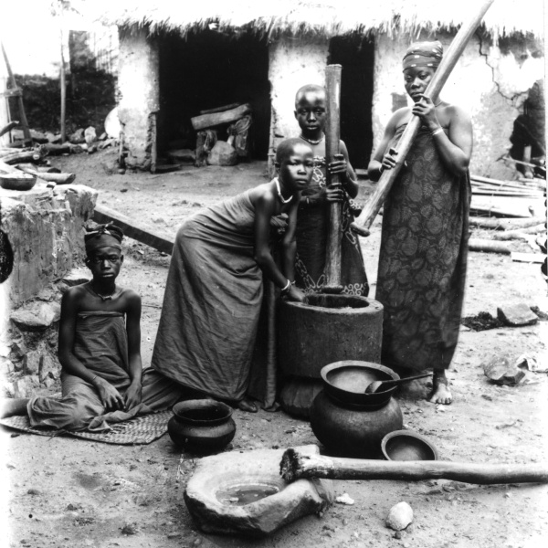 Fotografie. Ženy a dívky s tlouky v rukou kolem stoupy. Ghana (Zlaté pobřeží), 1885-1888. Zdroj: Národní muzeum