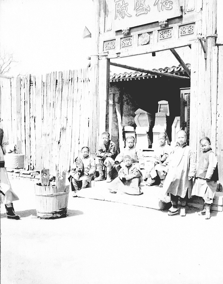 Fotografie. Skupina dětí před obchodem s rakvemi. Čína, Peking, 1901. Zdroj: Národní muzeum