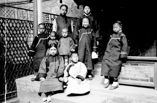 Fotografie. Skupina dětí mandžuských šlechticů na verandě domu. Čína, Peking, 1901. Zdroj: Národní muzeum