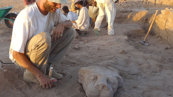 archeolog ve výjkopu nad nalezeným kamenným chrlicem v podobě hlavy lva